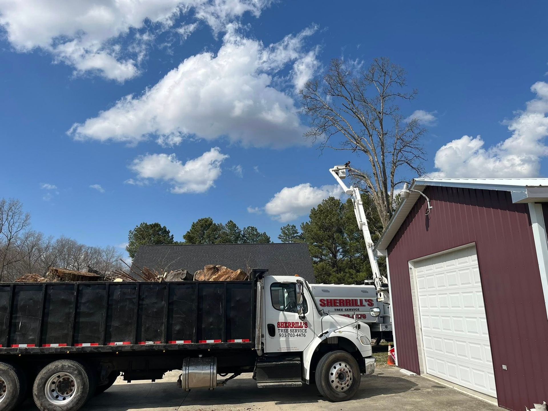 White dump truck beside a maroon garage under a blue sky with clouds