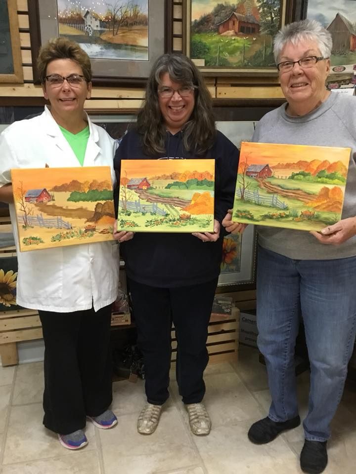 Three person are standing next to each other holding paintings.