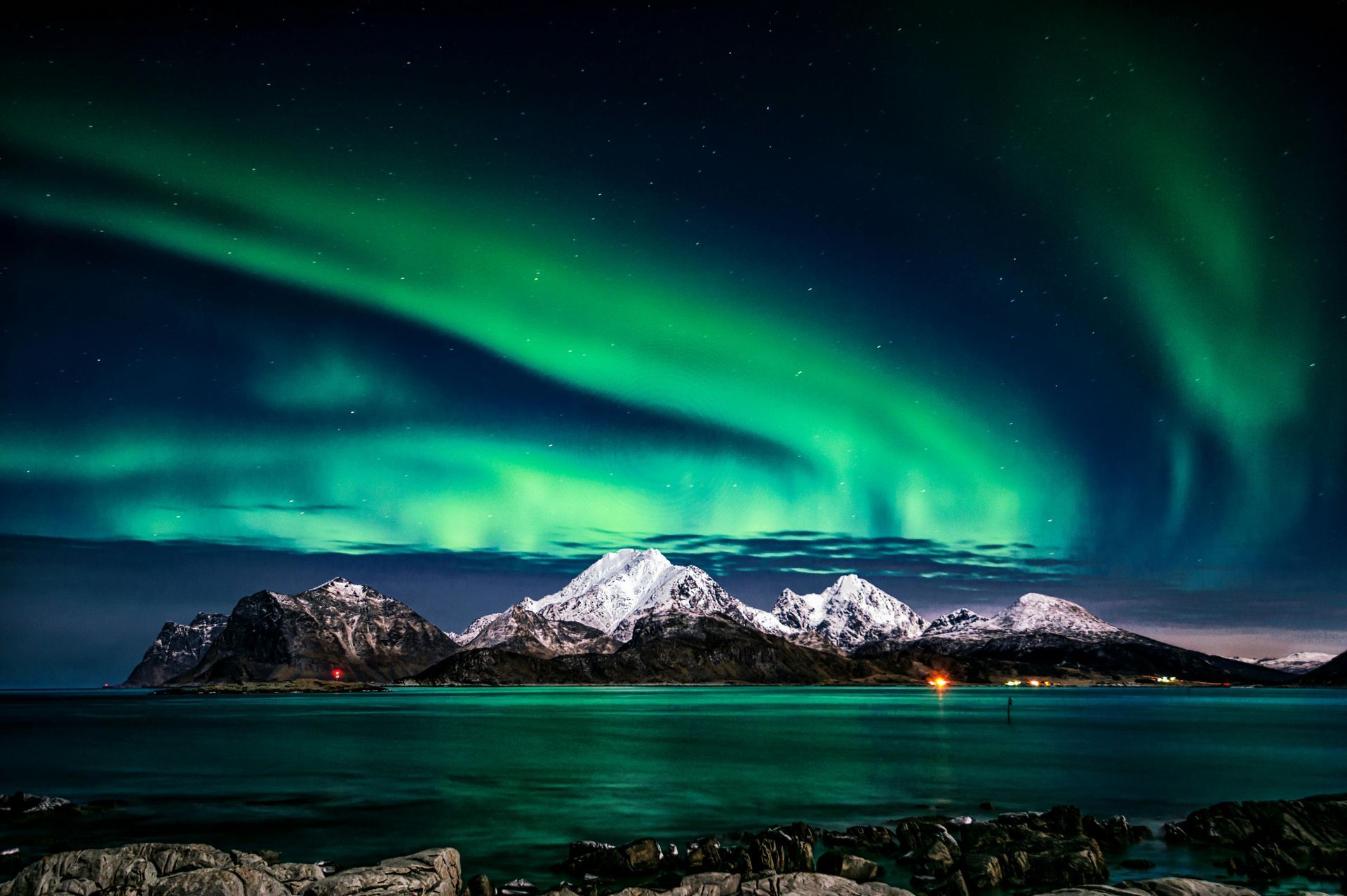 The aurora borealis is shining over the mountains and the ocean.