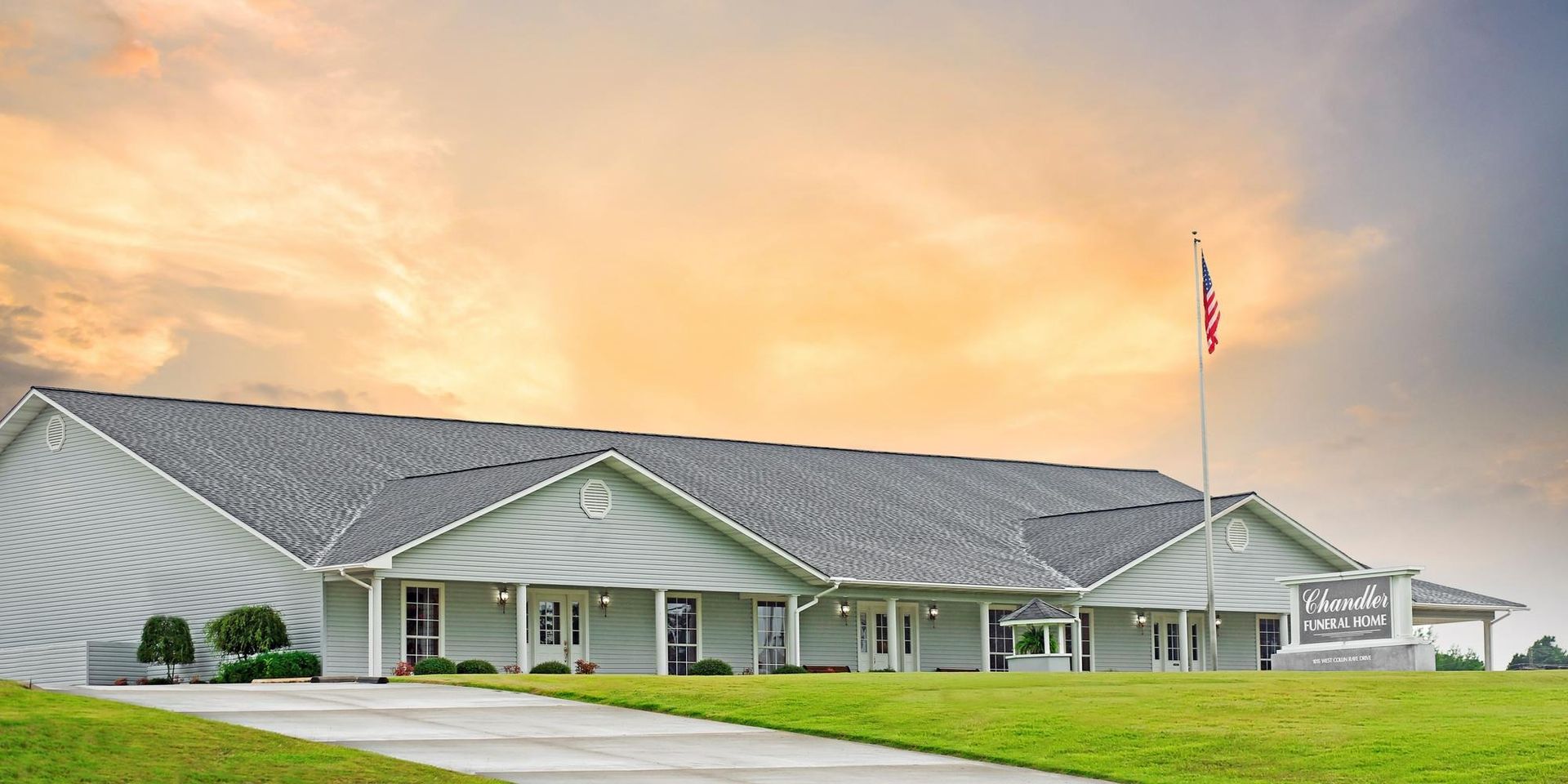 Single-story civic building with gray roof and an American flag at sunset