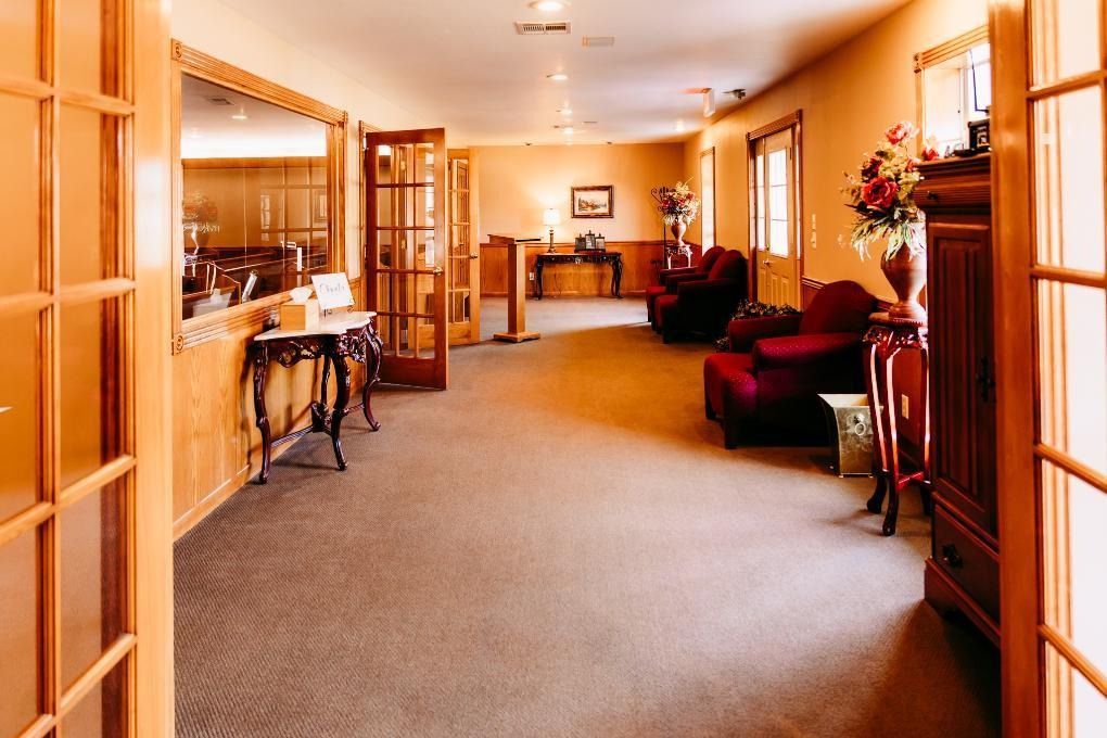Warm hallway with wood paneling, carpeted floor, mirrors, chairs, and floral decor in a home-like interior