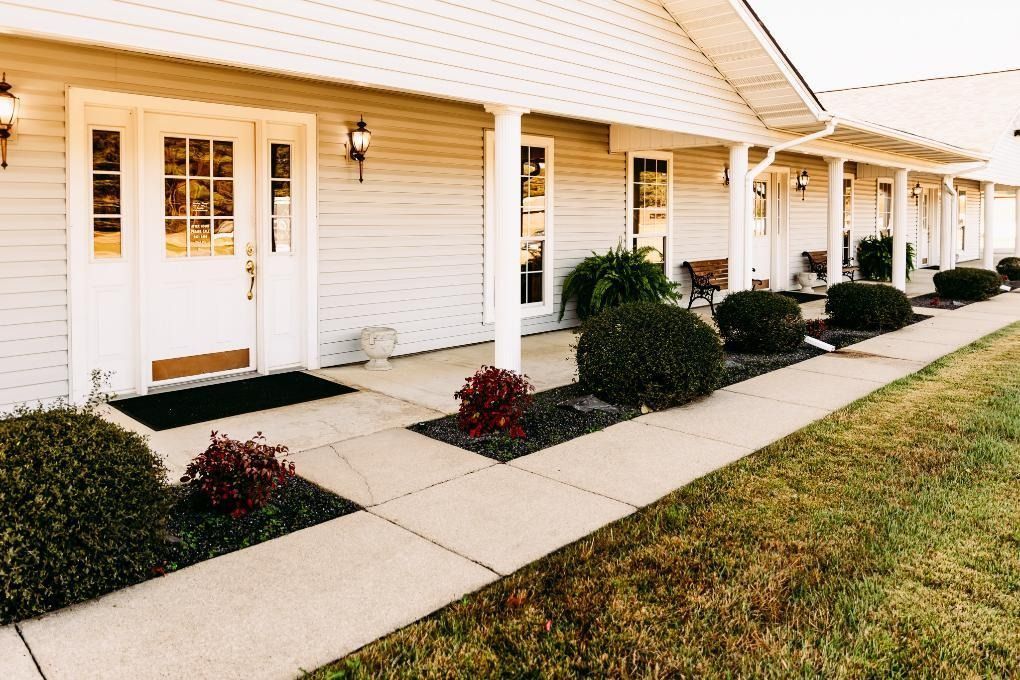 Row of white townhouse doors with small shrubs, concrete walkways, and a grassy lawn