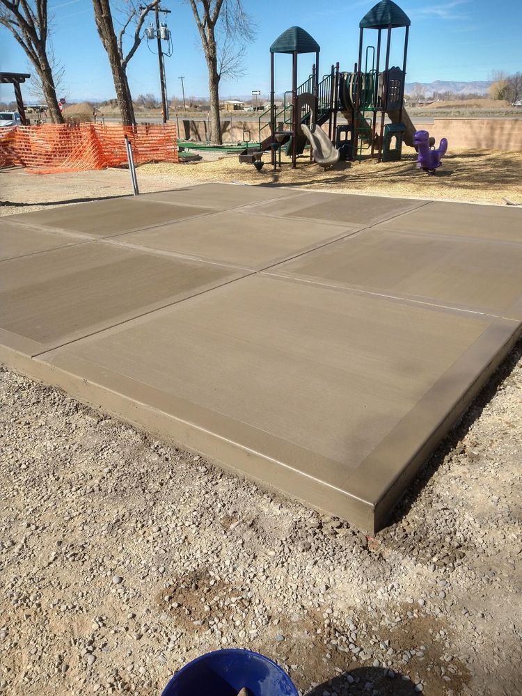 Newly poured concrete surface next to a playground with tan gravel ground.