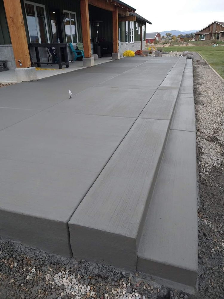 Newly poured concrete patio with steps leading down to a gravel area, next to a house with a covered porch.