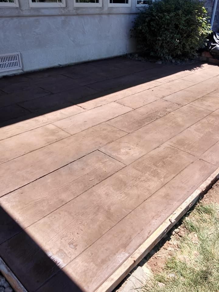 Brown stamped concrete patio, designed to look like wood planks, next to a building and grass.
