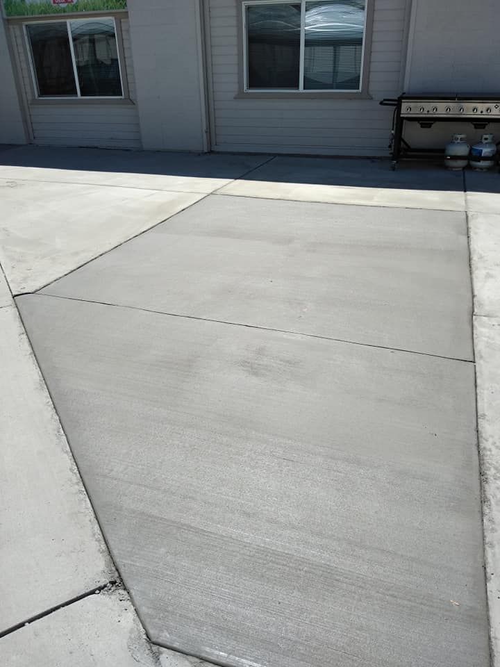 Freshly poured gray concrete slab bordered by existing concrete, outside a building.