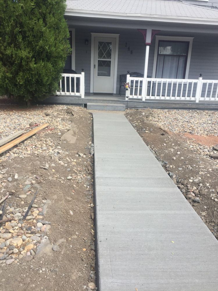 Newly poured concrete sidewalk leading to a light blue house with a white porch.