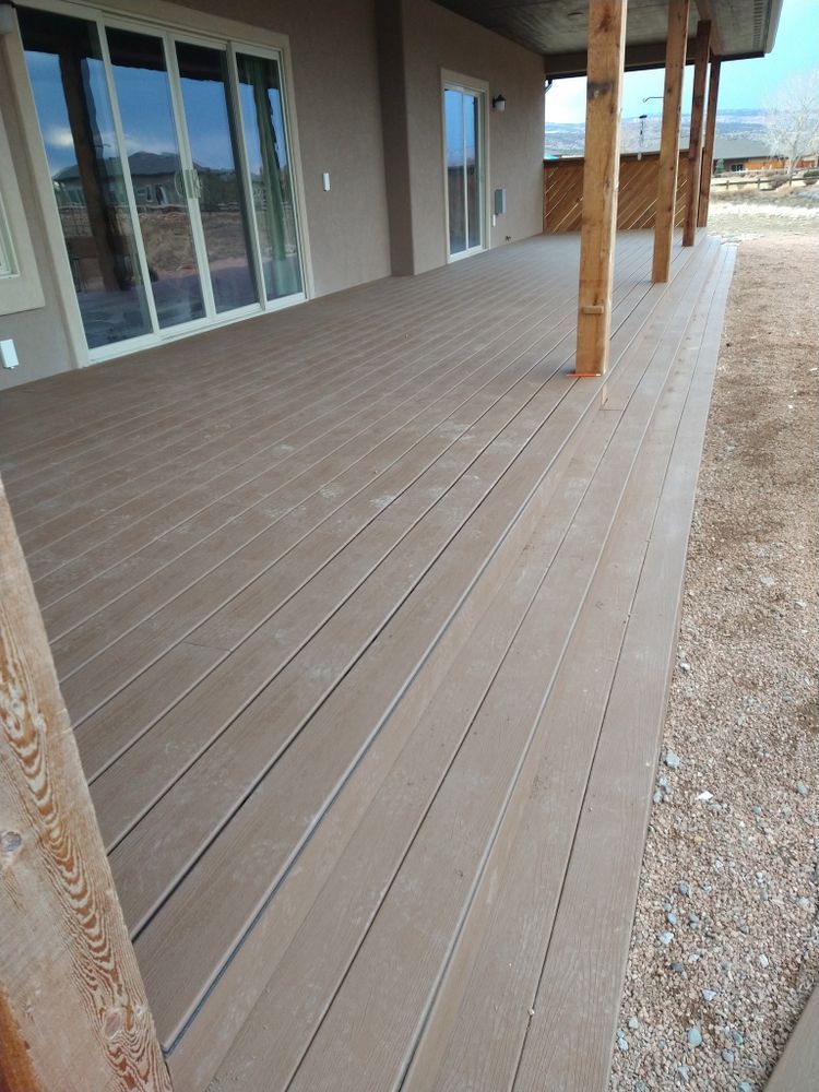 Brown composite deck with wooden support beams, extending from a tan building with glass doors.