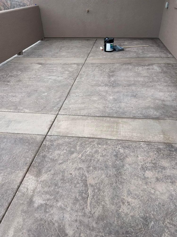 Concrete patio with dark grey textured finish, bordered by light brown walls and railing.