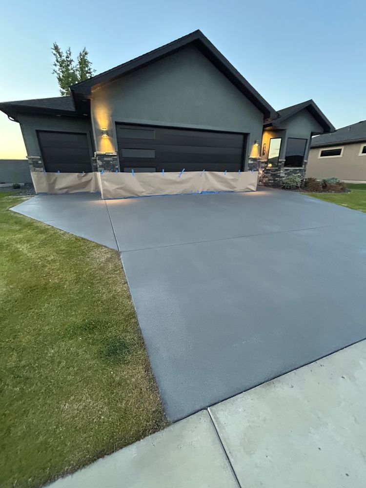 Gray concrete driveway leading to a modern house with a black garage door and green grass.