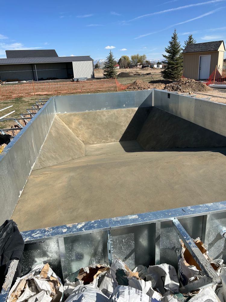 Empty rectangular pool under construction, metal frame with freshly poured concrete, outdoor setting.