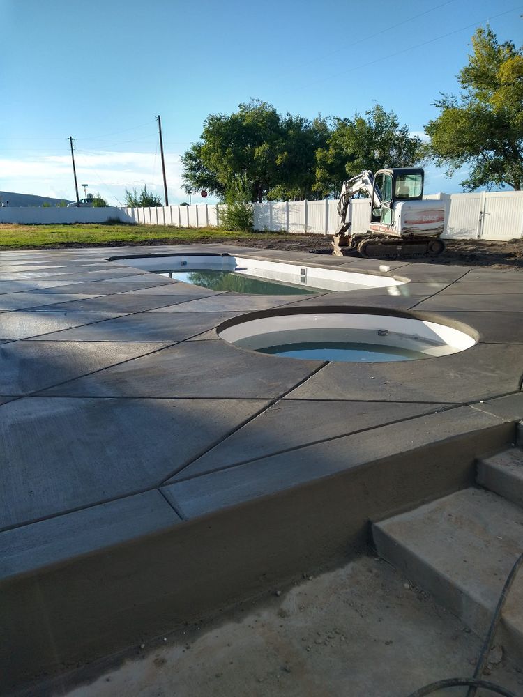 Concrete pool deck under construction with round spa openings, excavator in background.