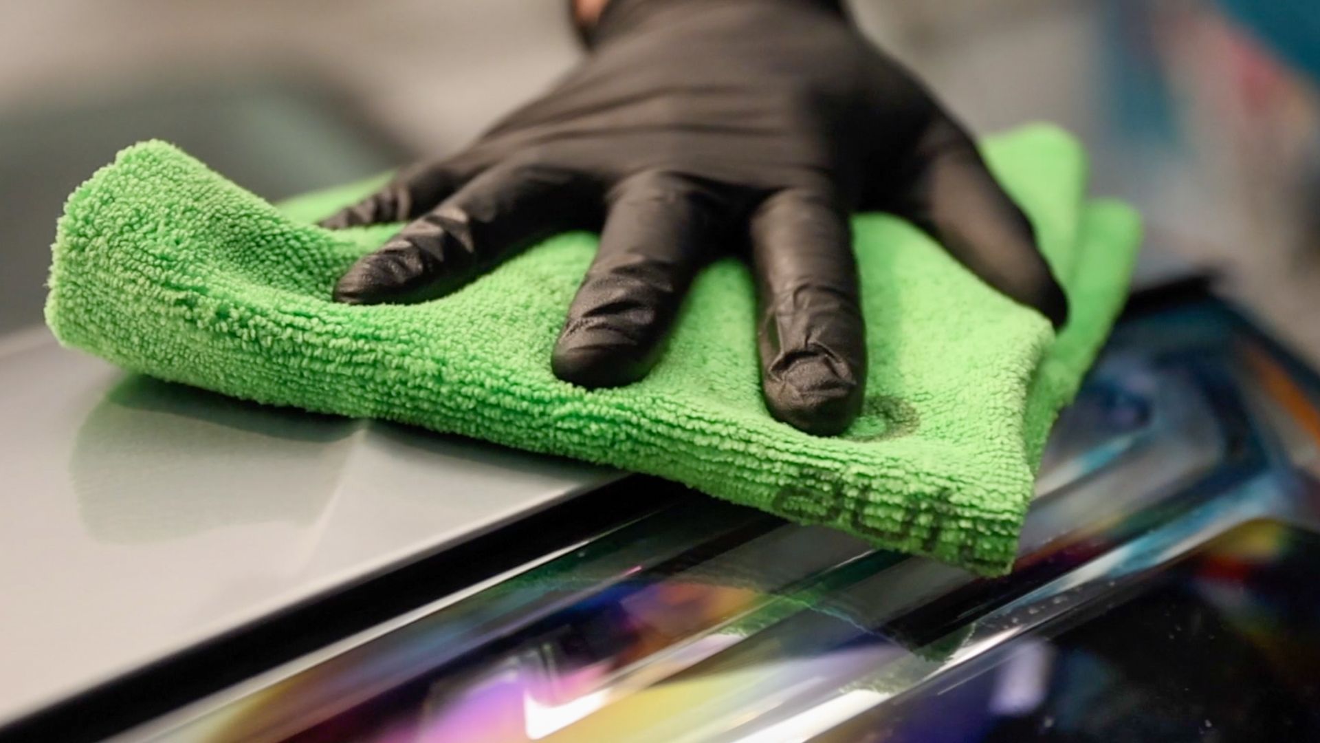 A person wearing black gloves is cleaning a car with a green towel.