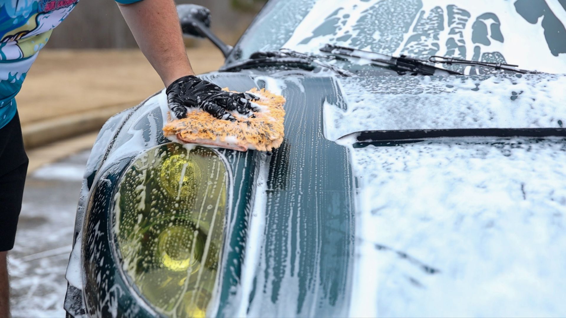 A person is washing a car with a sponge and foam.