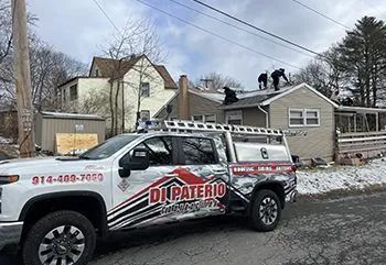 White truck with logo parked near a house, roofers working on the roof in a snowy setting.
