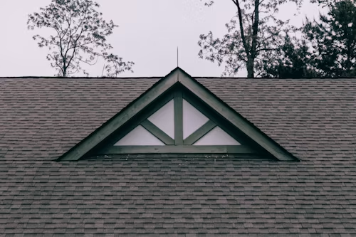 House roof with a triangular dormer window and trees in the background.