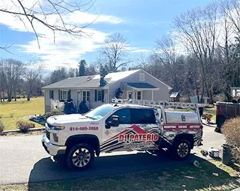 A truck is parked in front of a house with two men working on the roof.
