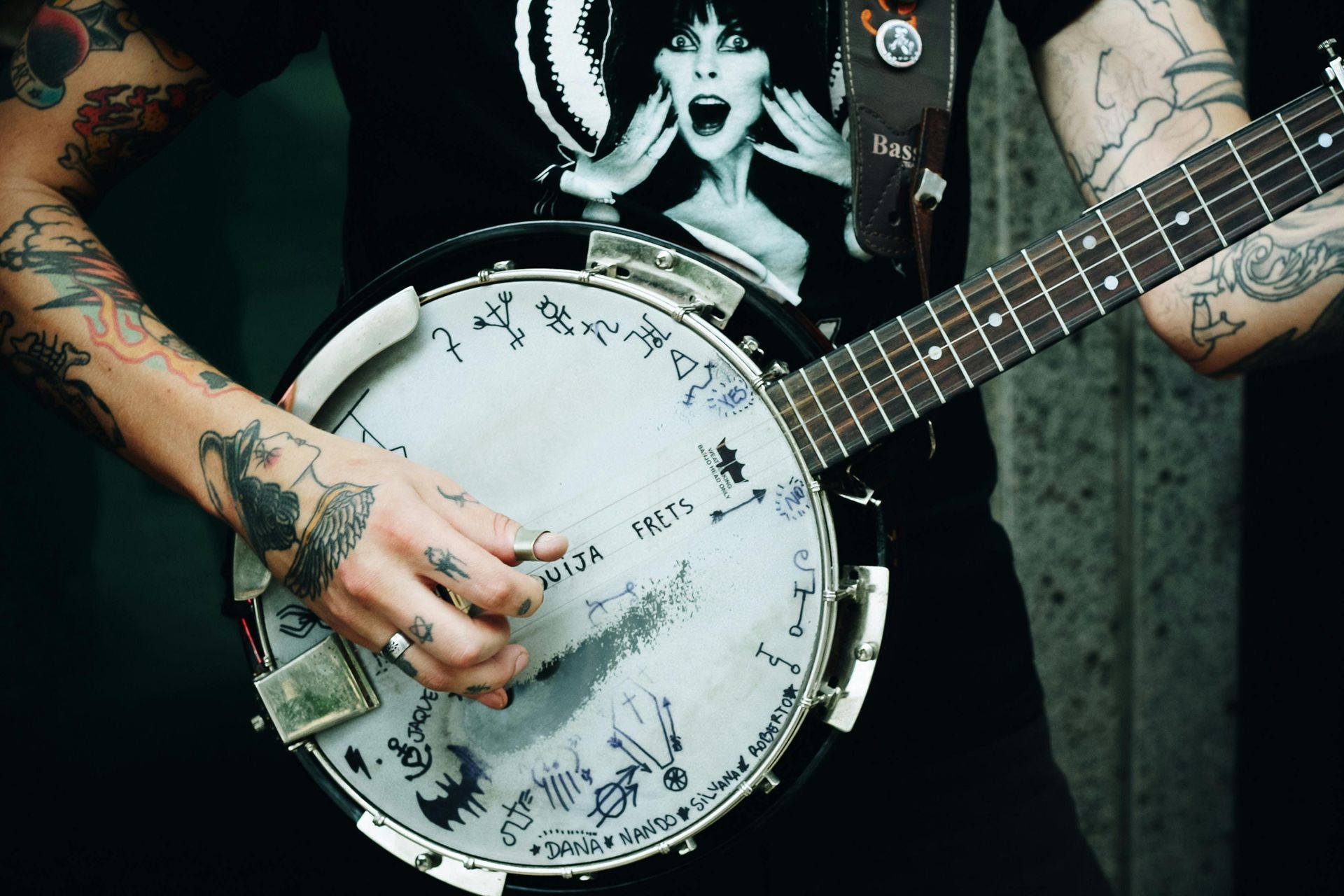 Tattooed musician playing a banjo, wearing a black graphic T-shirt.