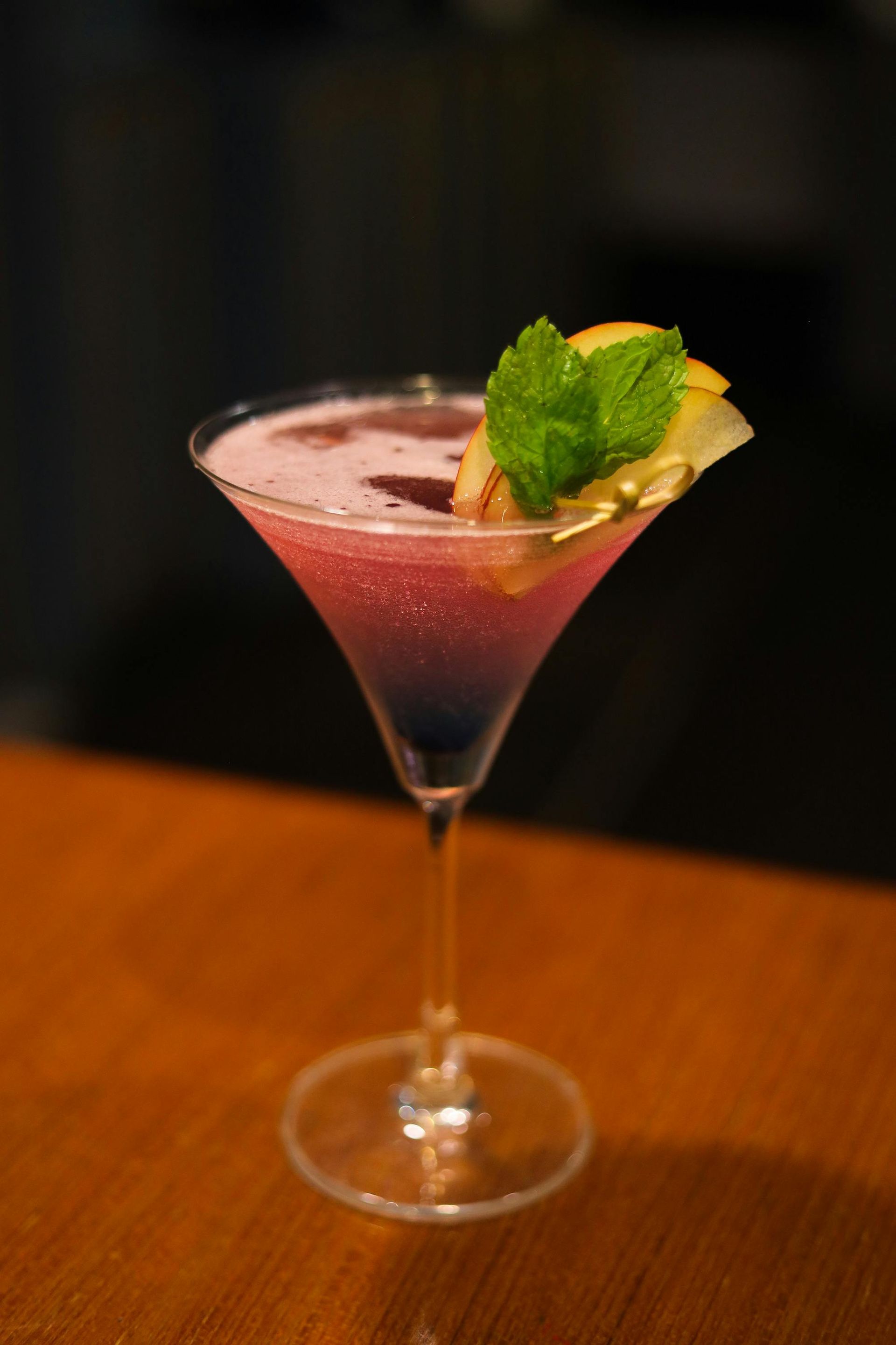 Pink cocktail in a martini glass, garnished with mint and citrus on a wooden table.