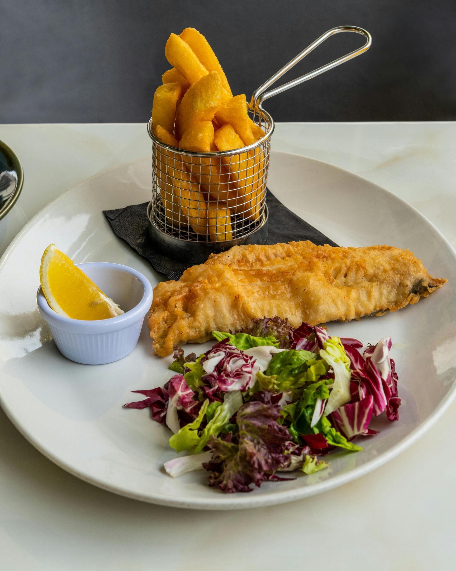 Fried fish fillet with chips in a metal basket and side salad on a white plate
