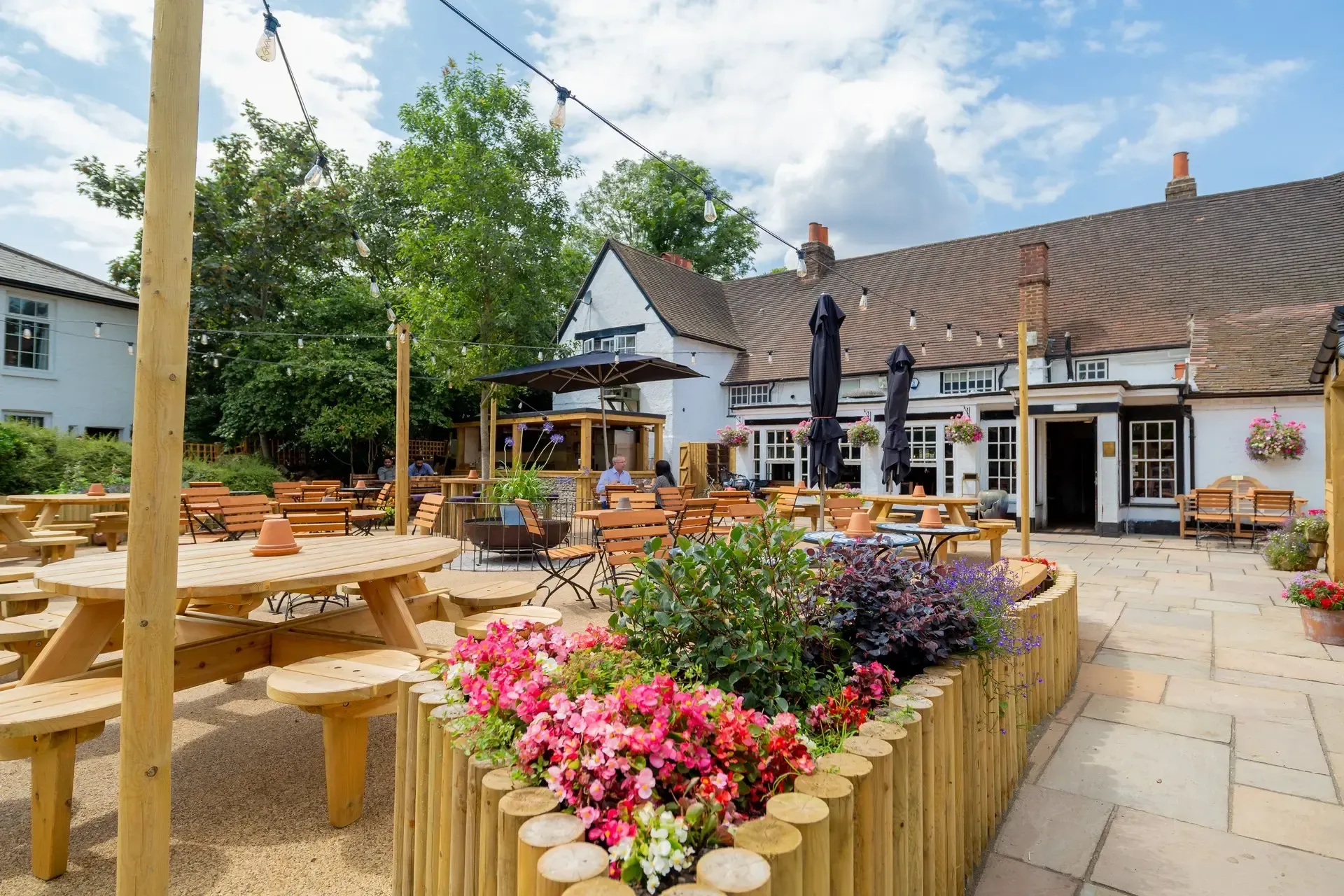 Flower-lined outdoor café patio with picnic tables and a rustic building under a blue sky