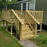A wooden deck and staircase built onto the side of an olive-green mobile home.