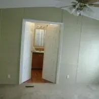 Open white double doors lead into a bathroom with a wood cabinet and a mirror, set in a room with light green walls.