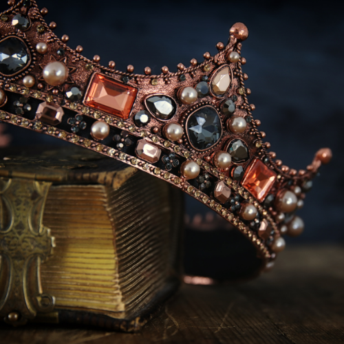 Copper-colored crown adorned with jewels and pearls, resting on a weathered book.