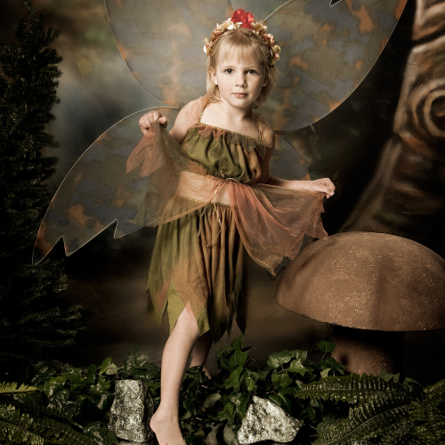 Young fairy costume model in green dress and pink wings standing in a forest setting