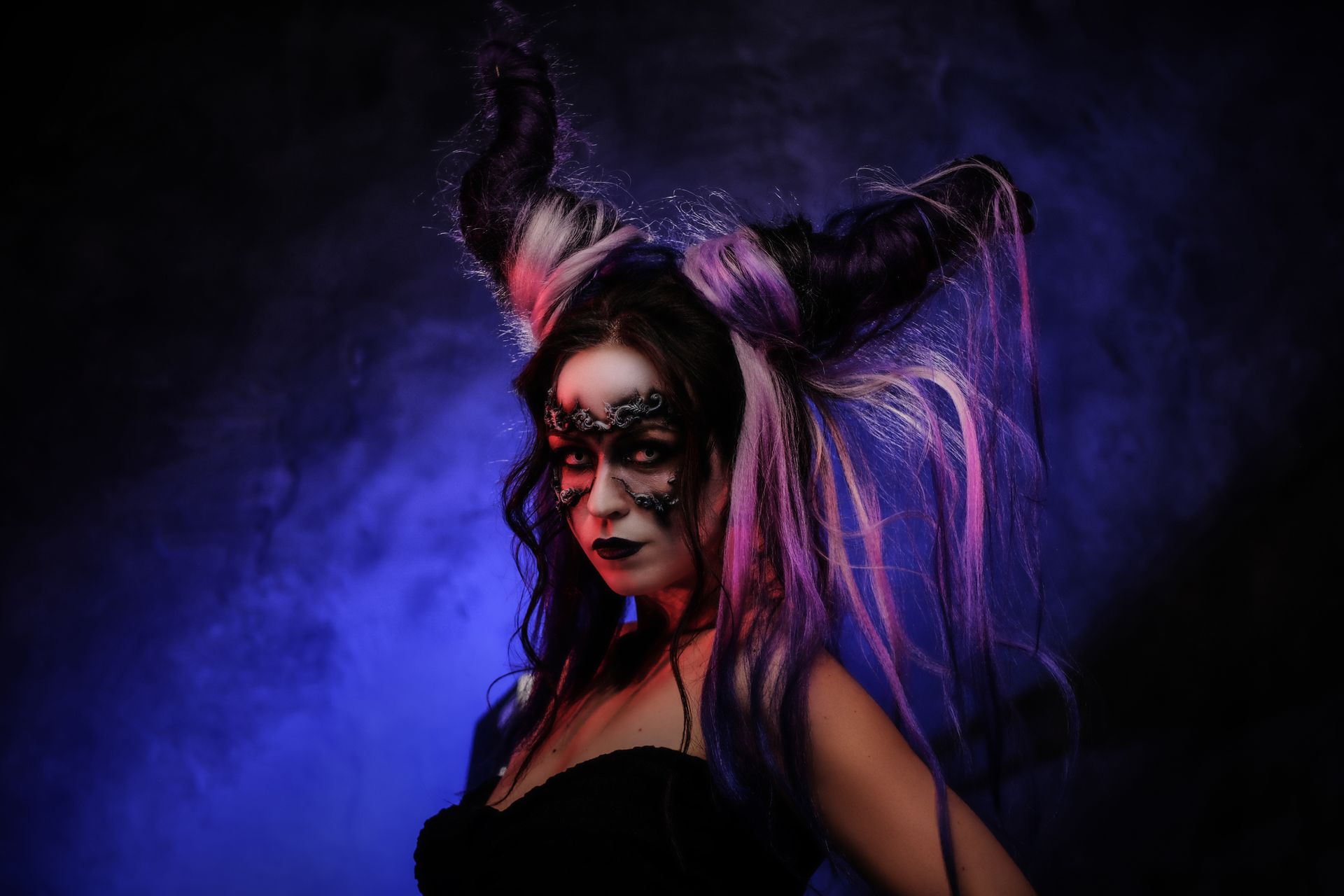 Woman in neon face paint and black outfit with purple hair against a smoky purple background