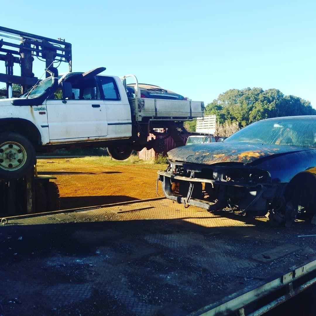 A White Truck Is Towing A Black Car On A Tow Truck — East Coast Metal Recycling In Redland Bay, QLD