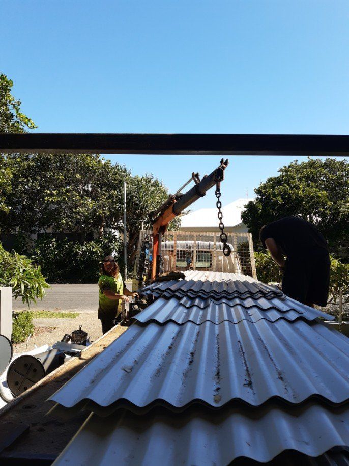 A Man Is Working On A Roof With A Crane — East Coast Metal Recycling In Tugun, QLD