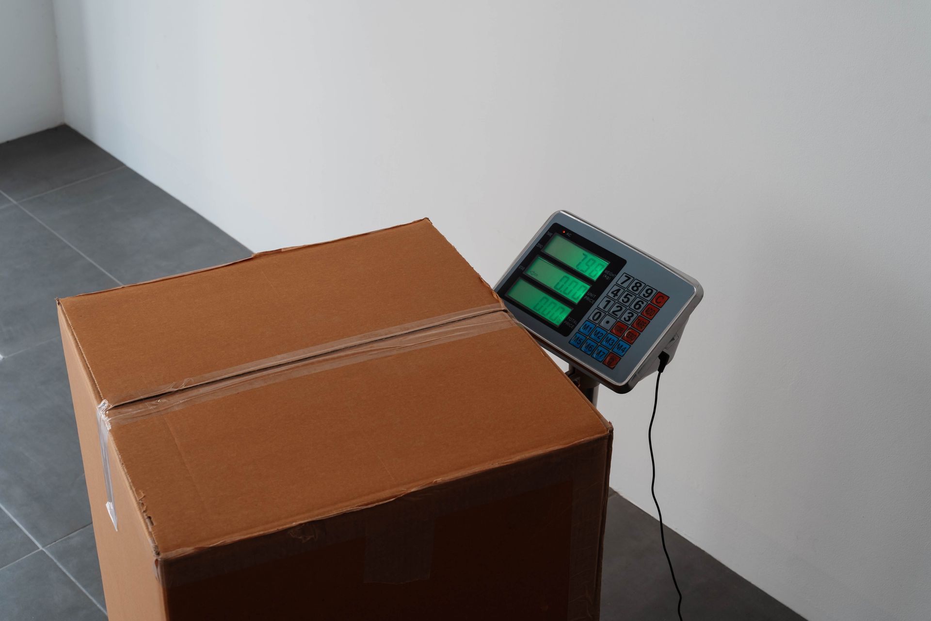 Sealed cardboard box sits on a digital platform scale with glowing green display indoors.