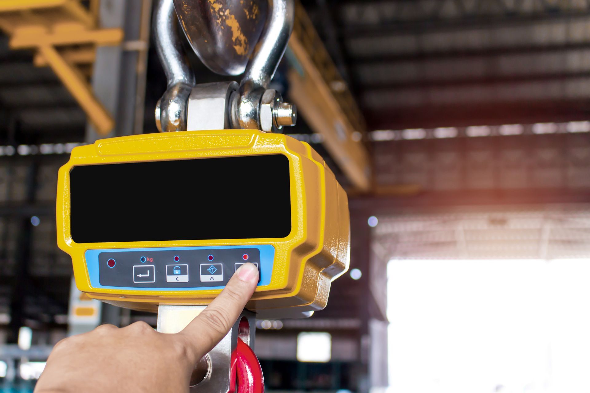 Industrial hanging crane scale with digital display and control buttons in a warehouse setting.
