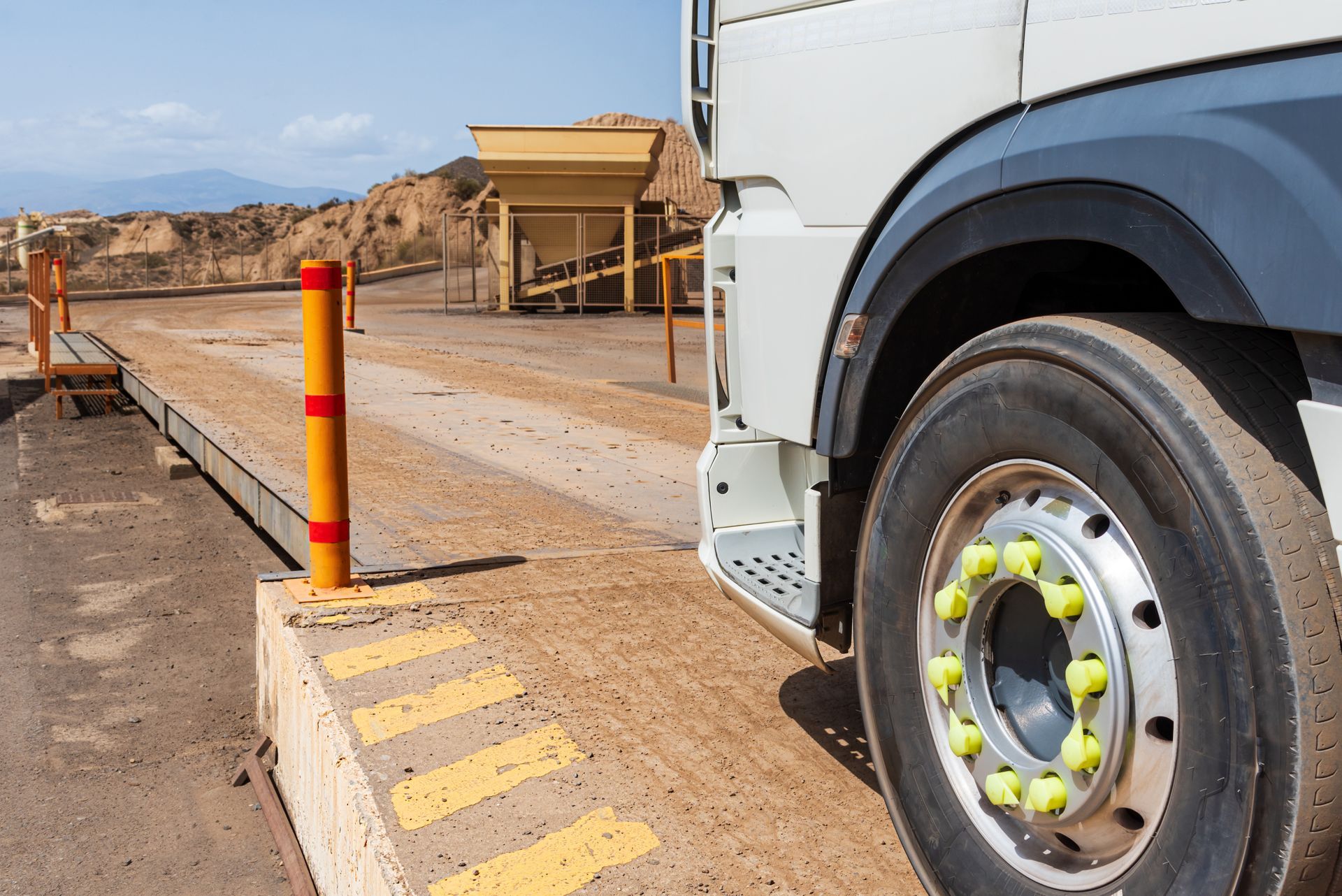 A truck pulls onto a metal scale platform at a dusty industrial site.