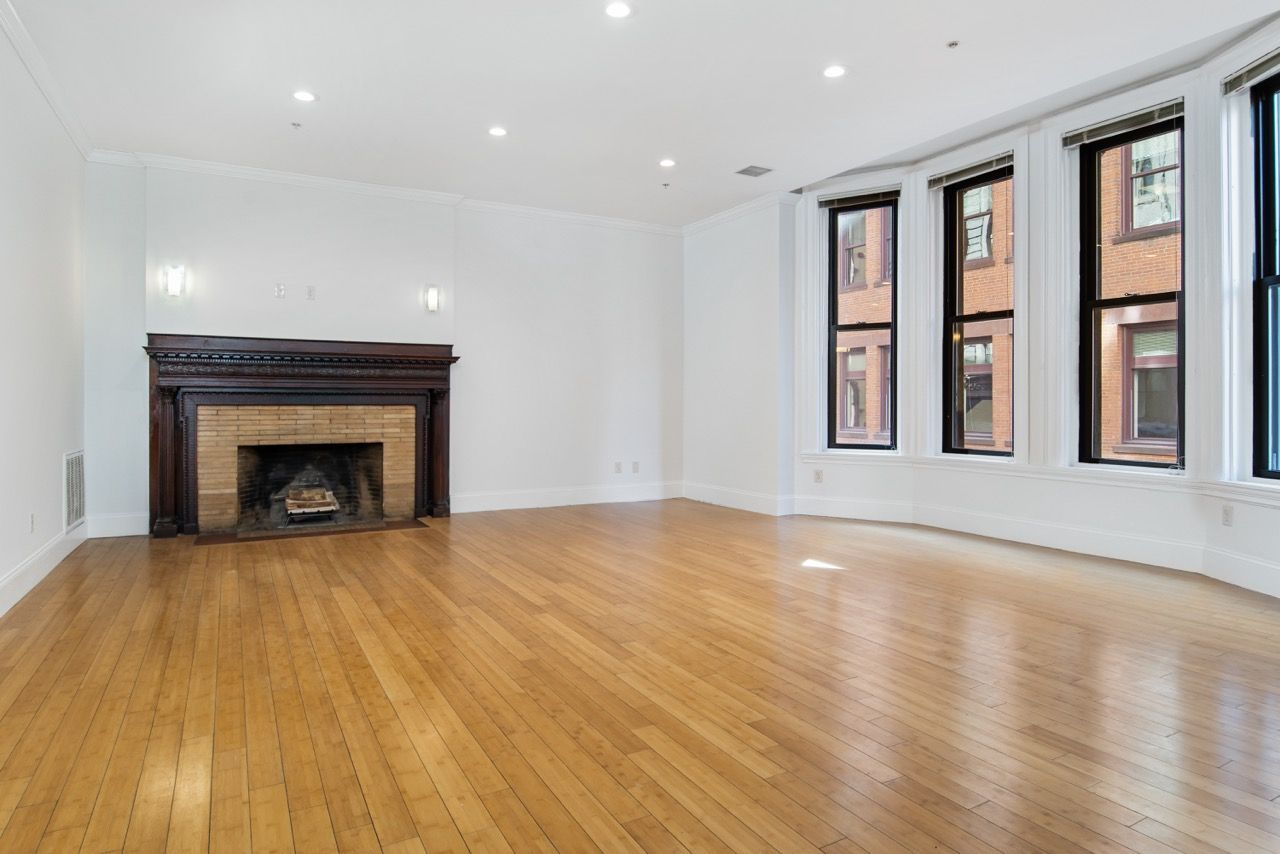 Bright living room with hardwood floors, a brick fireplace mantle, and large windows.