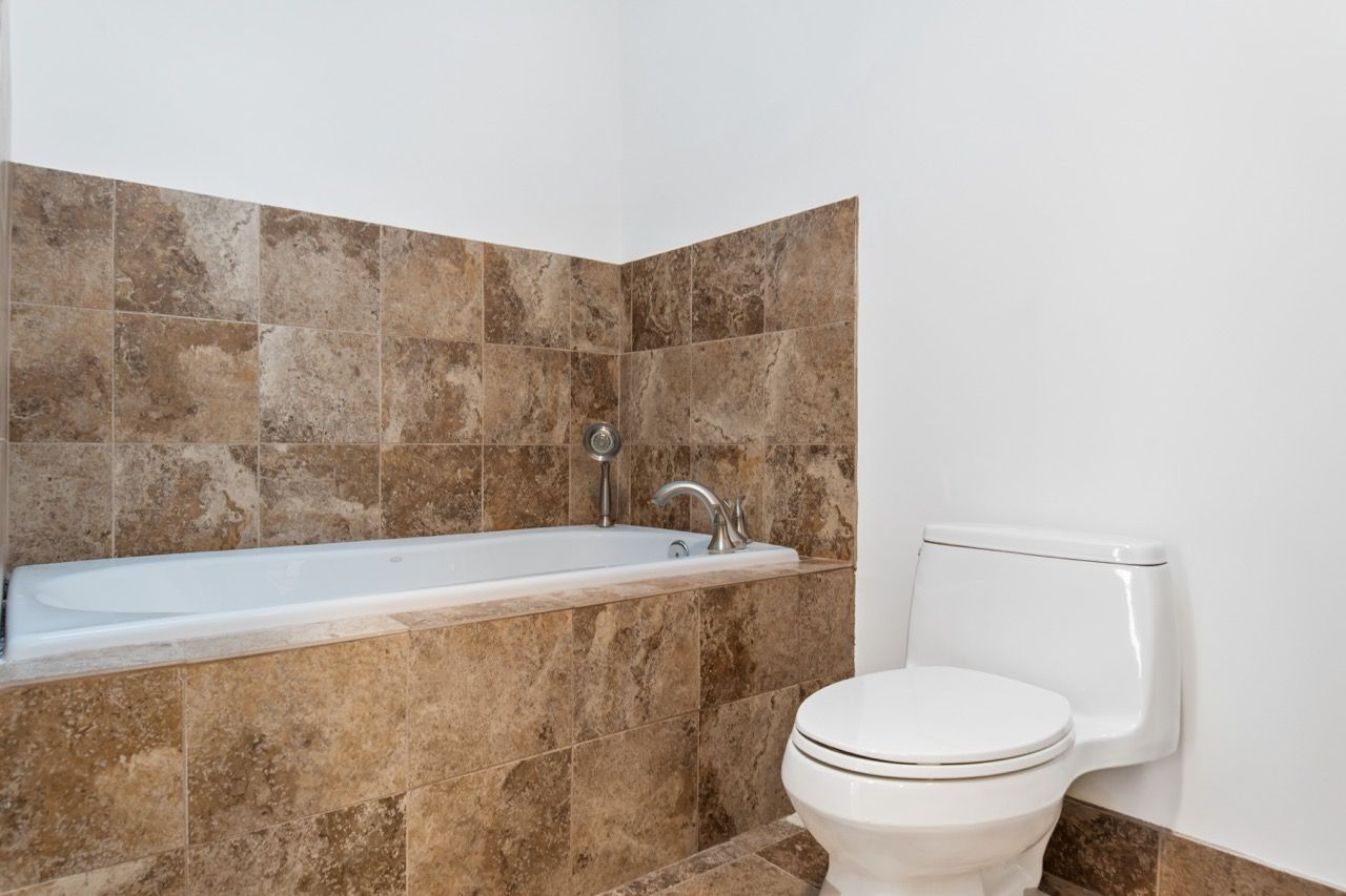 Bathroom with a white bathtub surrounded by brown tiled walls and a white toilet.