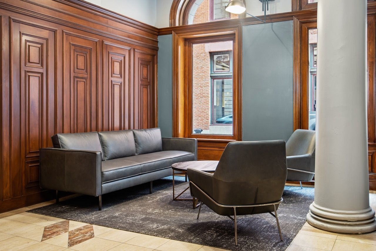 Wood-paneled lobby with gray sofa and chairs by large windows