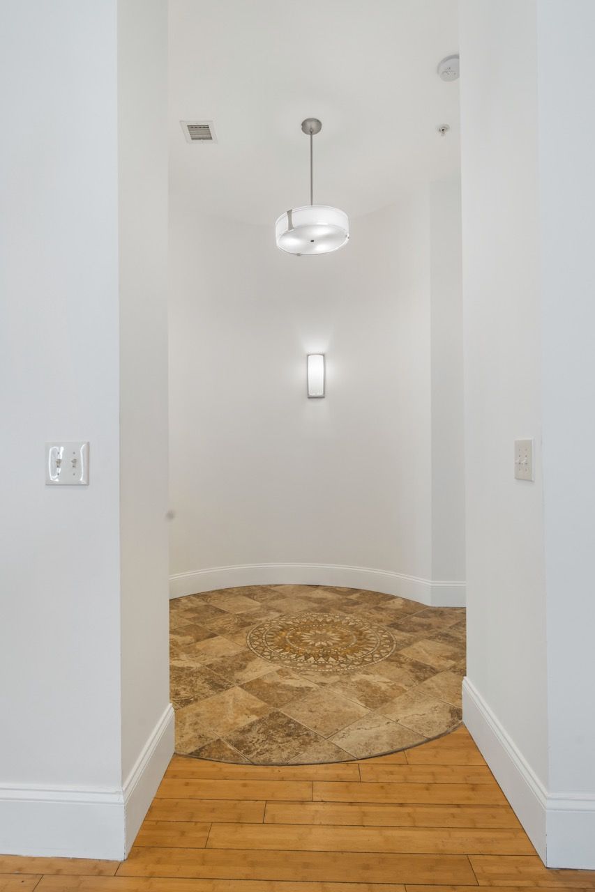 White entry foyer with curved tile mosaic floor, pendant light, and wall sconce.