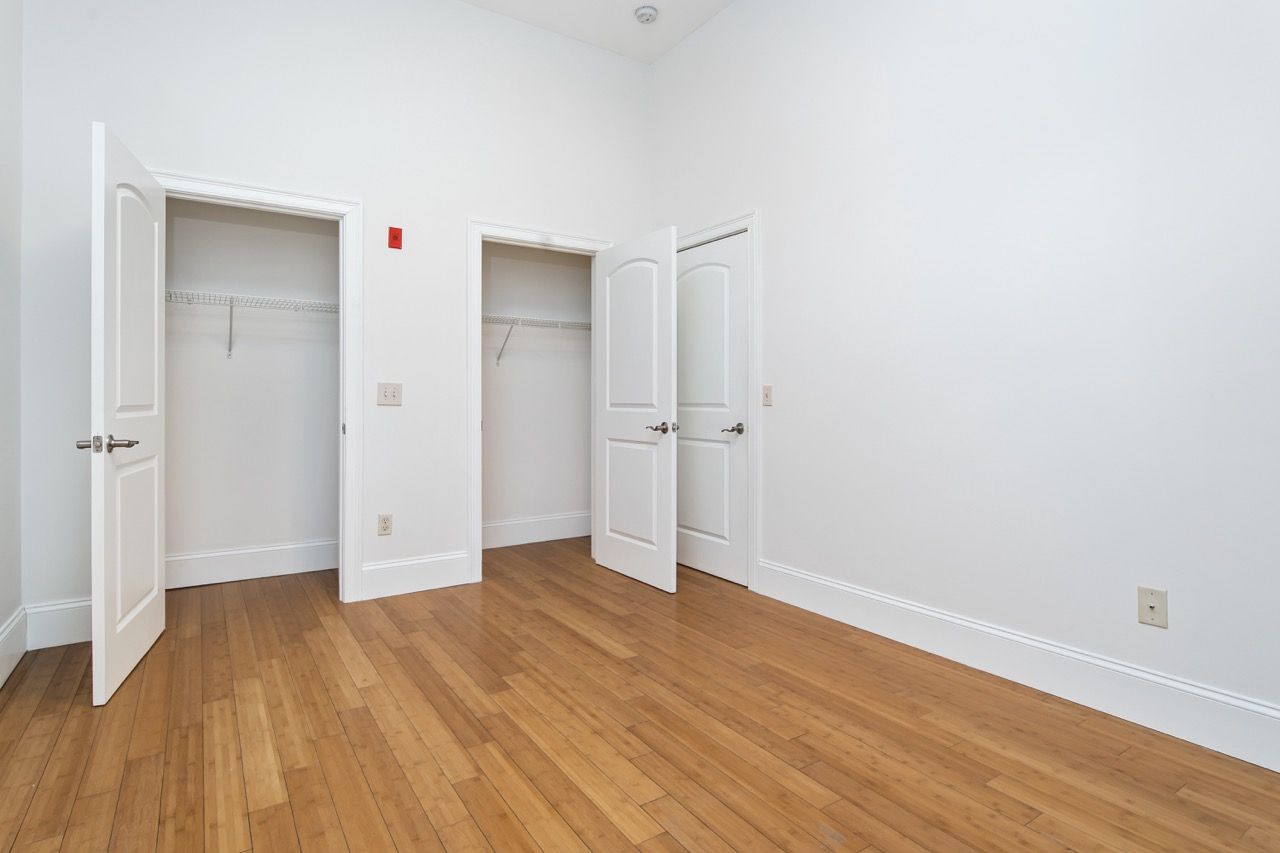 Empty bedroom with two open closets, light wood floors, white walls.
