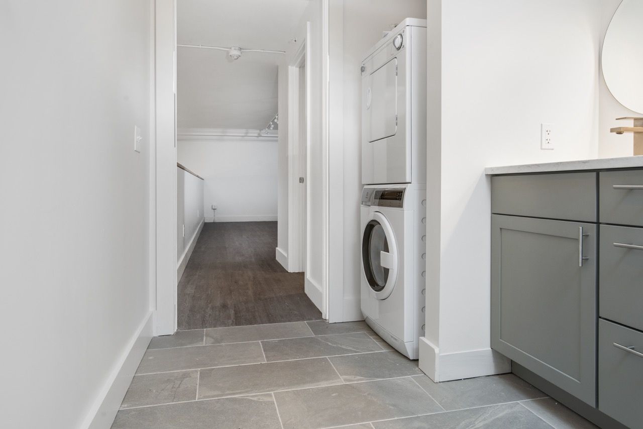 Laundry area with stacked washer and dryer next to gray kitchen cabinets.