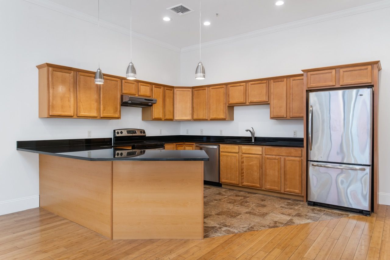 Kitchen in an apartment with wooden cabinets, black countertops, stainless steel appliances, and an island.