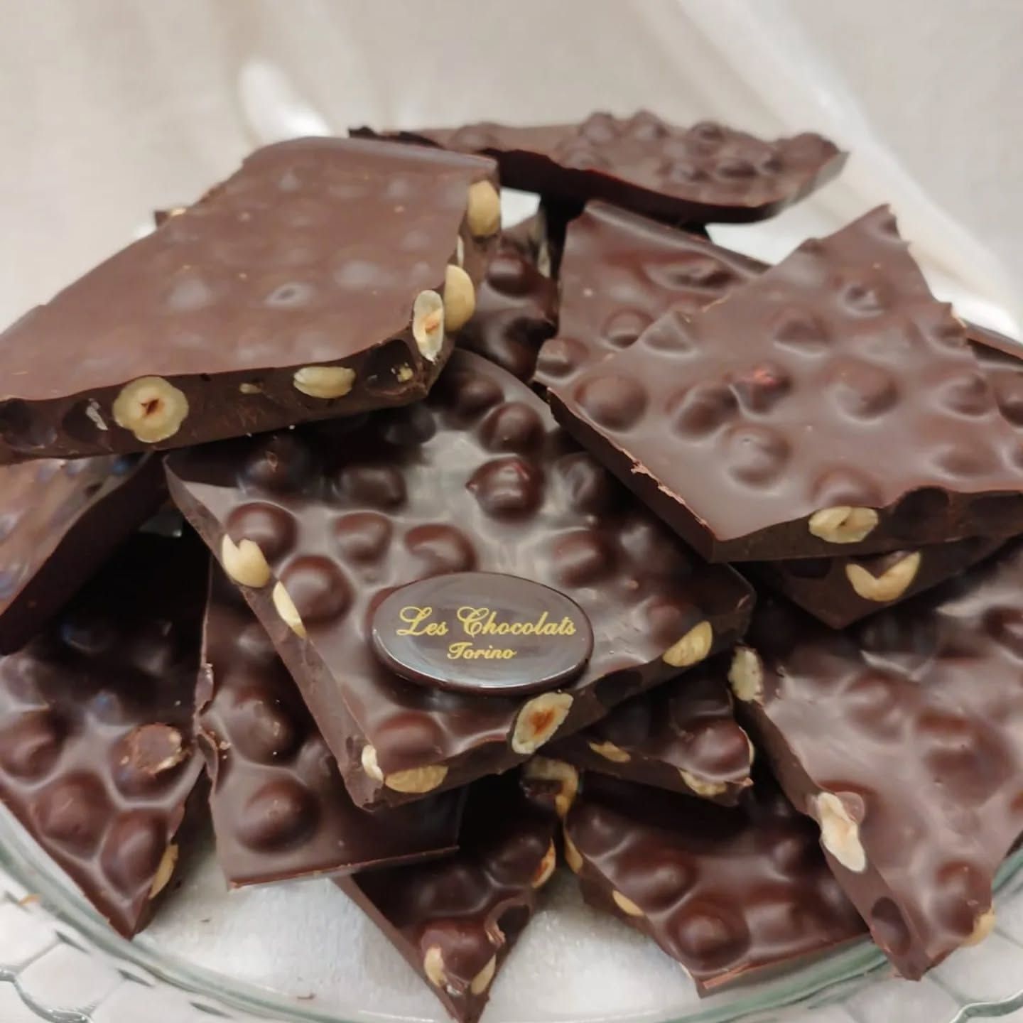 Scorza di cioccolato fondente con nocciole visibili in un contenitore di vetro.