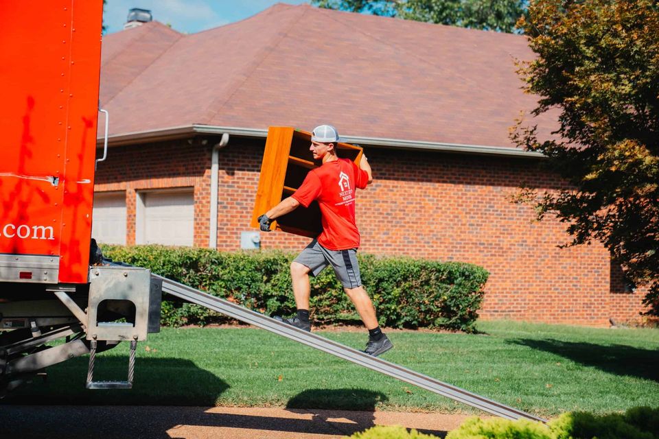 A man in a red shirt is carrying a couch down a ramp from a moving truck.