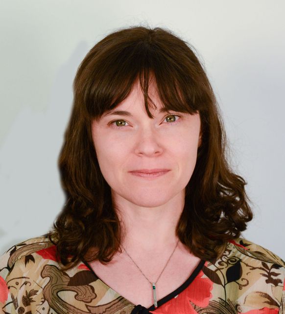 Woman with brown hair and bangs, wearing a floral top, looking at the viewer.