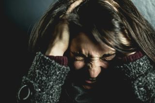 Woman with hands on head, eyes closed, showing distress.