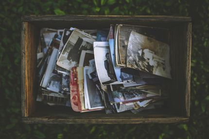 Wooden box overflowing with a pile of old, faded photographs; set on grass.