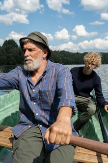 Man rowing boat with young man on a lake, sunny day.