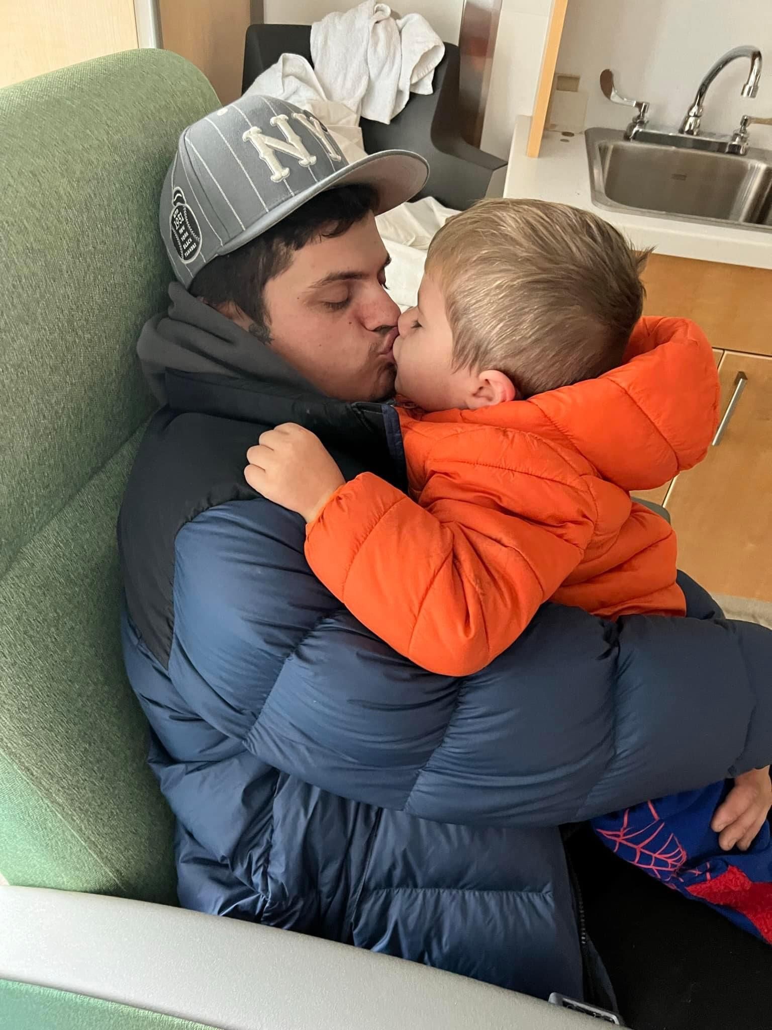 A man is kissing a child on the cheek while sitting on a couch.