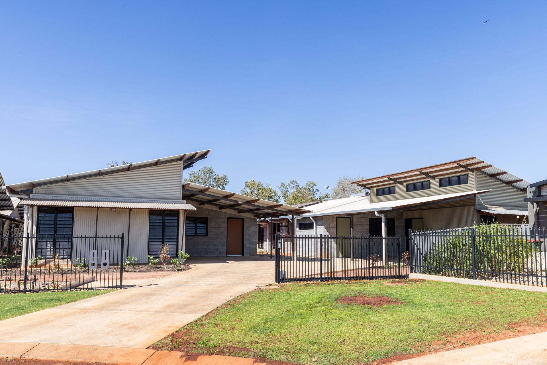 Two modern homes with angled metal roofs, blue sky, a driveway, and green lawn.